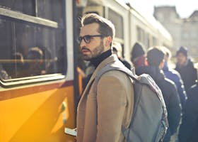 A stylish man with a backpack boards a tram in bustling Budapest, Hungary, during the day.